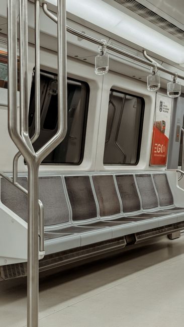 Interior view of a clean and well-maintained train carriage on Sidcup Station with upholstered fabric seats featuring a blue and red pattern along both sides of the aisle. Blue vertical handrails exte